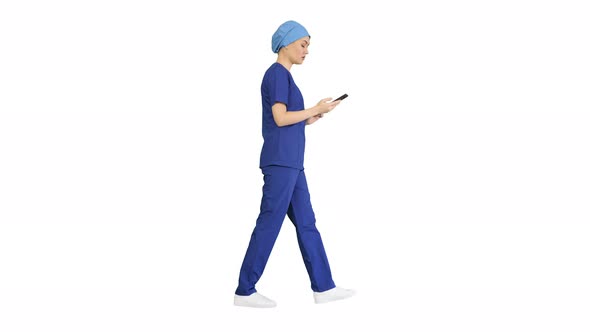 Female Doctor or Nurse in Blue Uniform Using Her Phone As She Walks on White Background