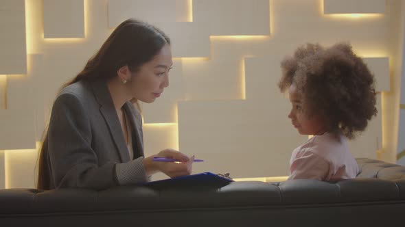 Asian Woman Counselor and Cute Little African Girl Sharing During Psychotherapy