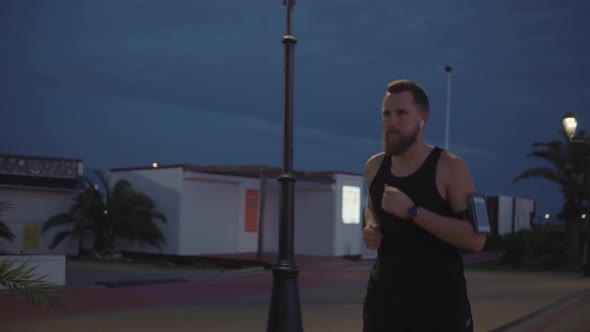 Tired Male Runner Is Jogging and Stopping in City Park in Evening, Resting