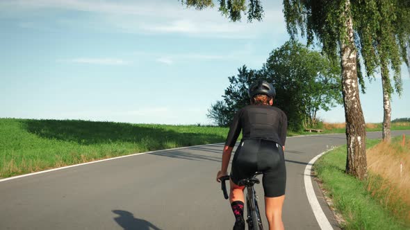 Professional female cyclist with muscular and fit body pushing pedals uphill out of saddle