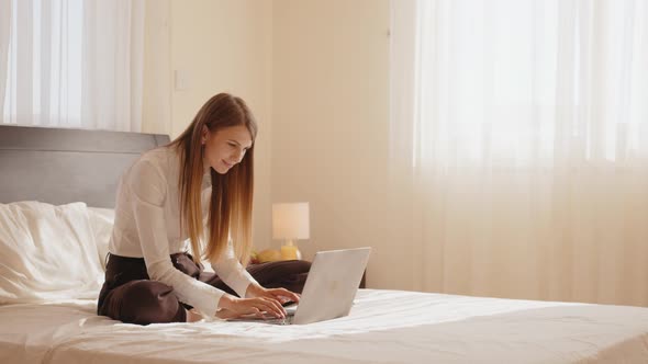 Smiling Woman Sitting on Bed and Using Modern Laptop