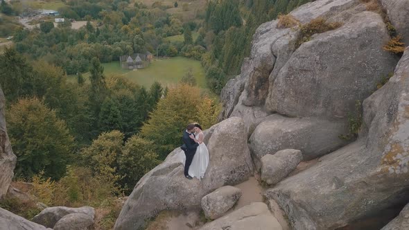 Newlyweds Stand on a High Slope of the Mountain, Groom and Bride. Aerial View