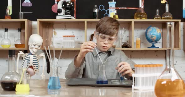 Laboratory Experience in a Chemistry Lesson, Boy in Protective Glasses Pours a Blue Liquid