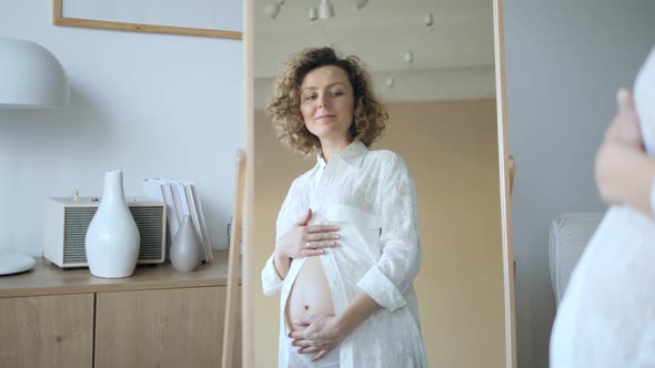 Beautiful Pregnant Woman Looking In Mirror While Touching Her Belly