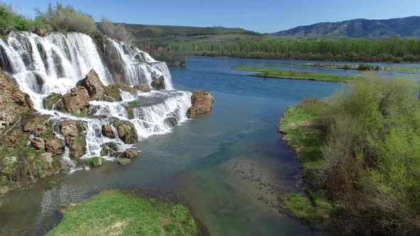 Flying view of waterfall flowing over edge into river