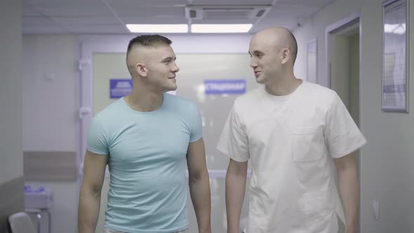 Two Positive Caucasian Men Walking Along Hospital Corridor and Talking. Portrait of Happy Patient