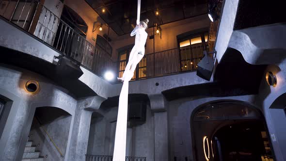 Female aerialist performing a headlong drop on silks in a club venue.