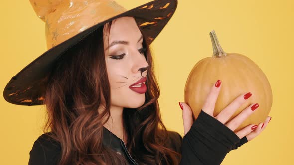 Woman in Halloween Makeup Holding Pumpking on Orange Background