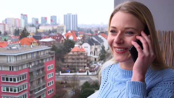 A Young Beautiful Woman Stands on a Balcony and Talks on a Smartphone - Closeup