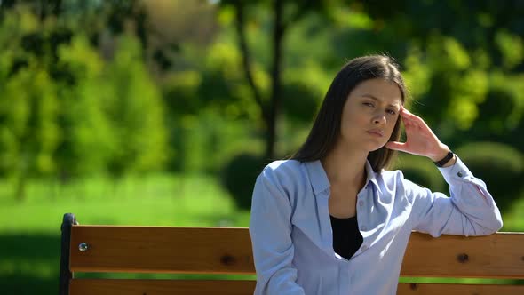 Tired Woman Resting on Bench Massaging Temples, Feeling Headache, Migraine