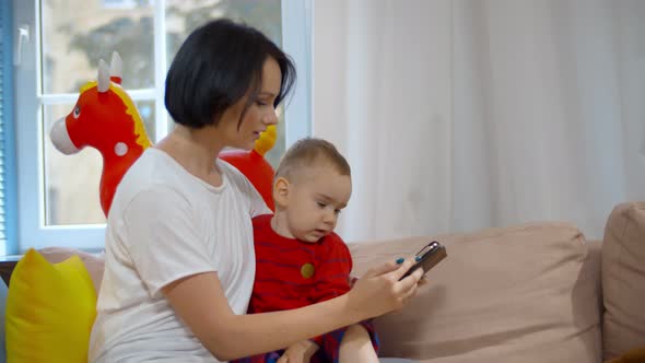 Caucasian Mother and Son Sitting on Sofa and Using Mobile Phone