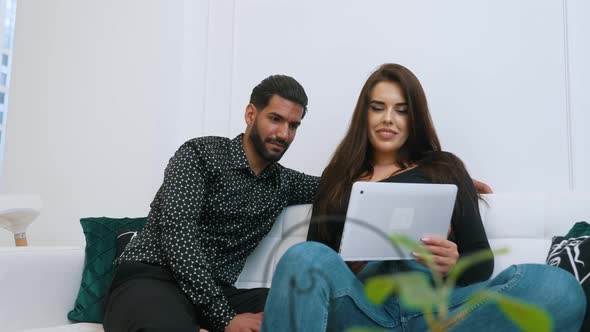 Handsome Bearded Cuban Man in Patterned Black Shirt Sitting on a Sofa with His Beautiful Longhaired