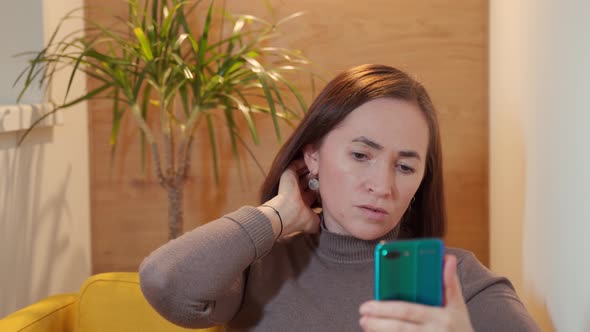 Happy Woman Sits in a Chair and Chats on Social Networks Using Mobile Phone Smartphone