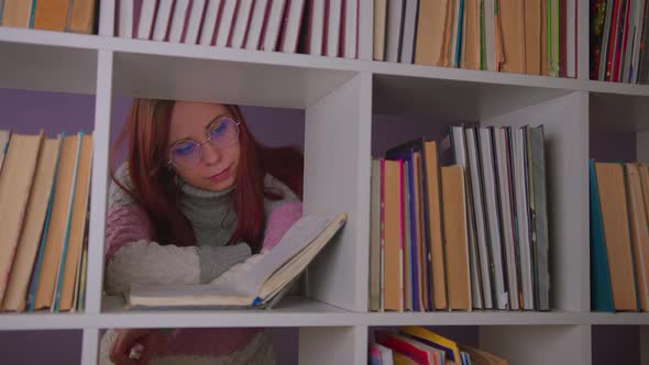 A Student is Reading a Book in the Library Behind the Bookshelves