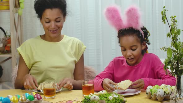 Mom and Daughter with Funny Bunny Ears are Drinking Tea with Easter Cake