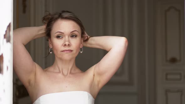 a Gentle Attractive Woman in a White Dress with Bare Shoulders at an Open Window