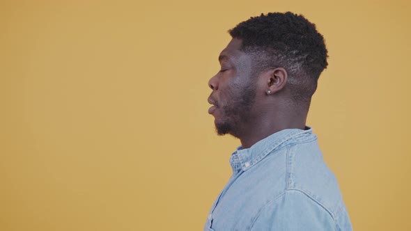 Young AfroAmerican Man in Blue Shirt Sighs Looking Away Yellow Background Studio Shot Copy Space