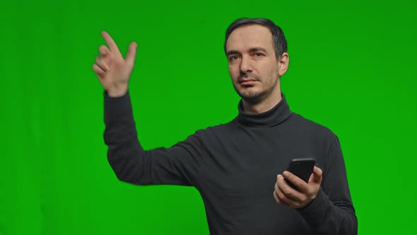 Man Holds the Phone in His Hands and Points to the Side on Isolated Green Background