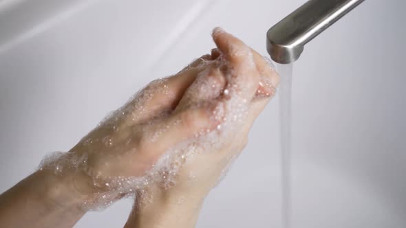 A Woman Washes Her Hands with Soap Over a White Sink To Eliminate Germs and Protect Against the