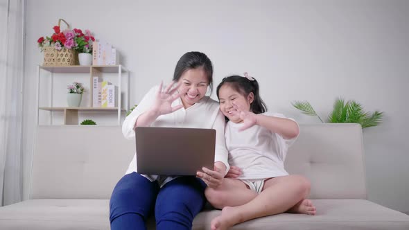 lovely asian mom and daughter sitting on sofa and taking vdo call with grandmother in living room