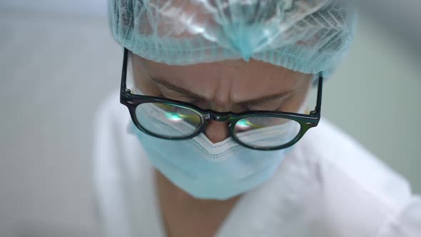 Closeup Face of Focused Dentist in Face Mask and Eyeglasses Working Indoors in Hospital