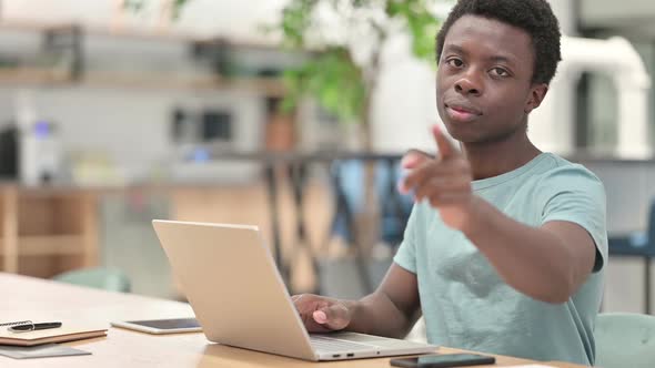 Young African Man with Laptop Pointing at the Camera