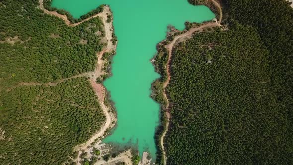 Turquoise water in a mountain forest lake with pine trees. Aerial view of blue lake and green forest