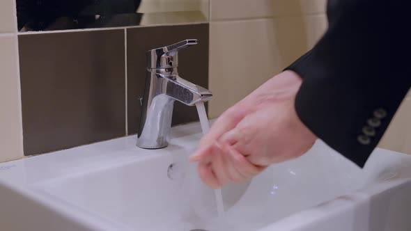 A man in a jacket washes his hands in a public toilet of a cafe