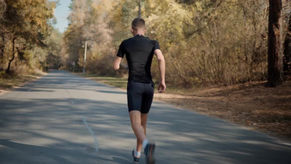 Running Man In Forest At Sunset. Runner Man Fit Athlete Legs Jogging On Trail Ready Triathlon.