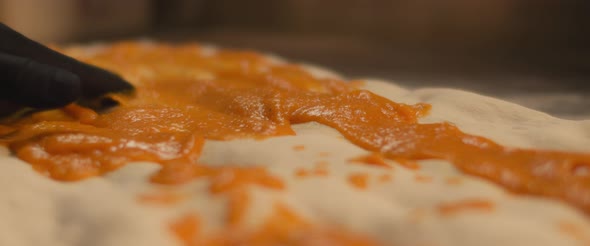 Chef spreading special pumpkin sauce over a fresh pizza al taglio dough. Close up, slow motion.