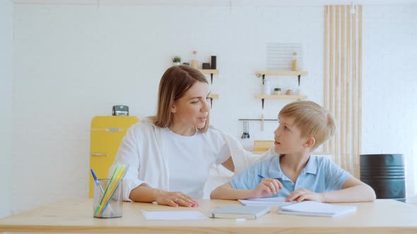 Mother and Her Son Schoolboy Do Homework Together at Home Sitting By the Table