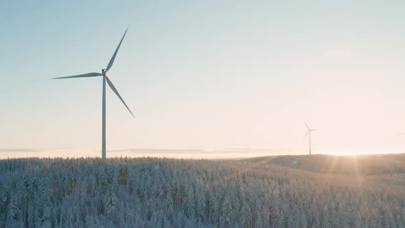 AERIAL - Wind turbines in a snowy forest at sunrise in Sweden, wide circle shot