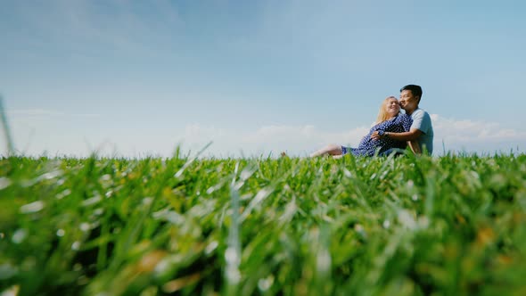 Asian Man with a Pregnant Woman are Resting in Nature in a Picturesque Place Sit on the Green Grass