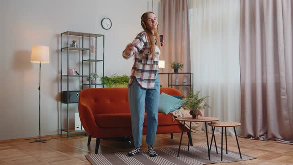 Overjoyed Young Woman in Wireless Headphones Dancing Singing on Cozy Couch in Living Room at Home