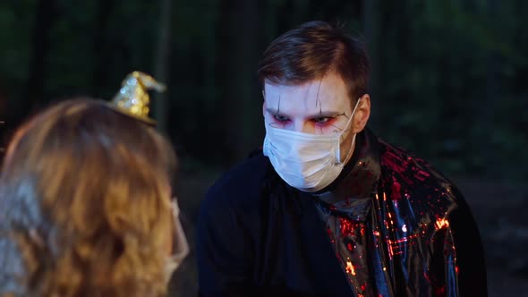 Portrait of Young Man in Vampire Costume with Face Paint in Coronavirus Face Mask Celebrating