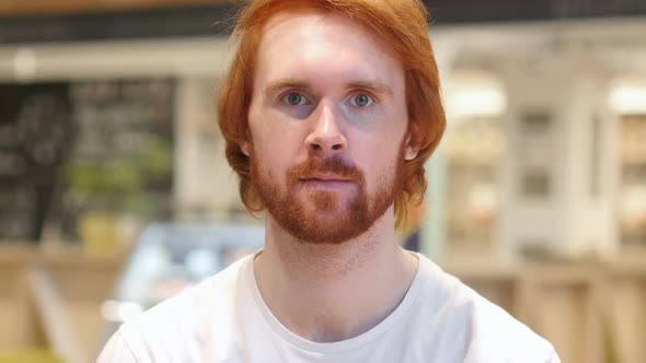 Serious Redhead Beard Man Looking at Camera in Cafe