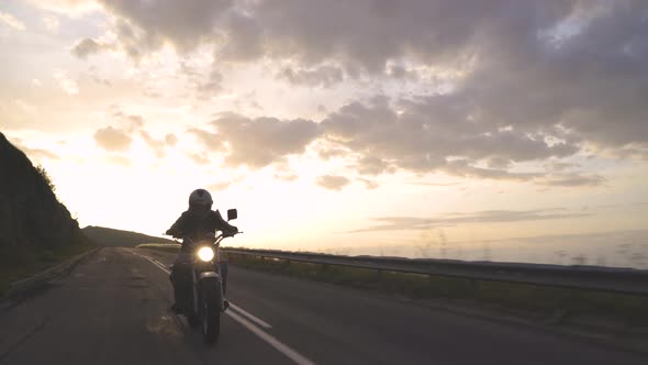 Carefree Man Riding His Motorcycle on Mountain Asphalt Road at Sunset