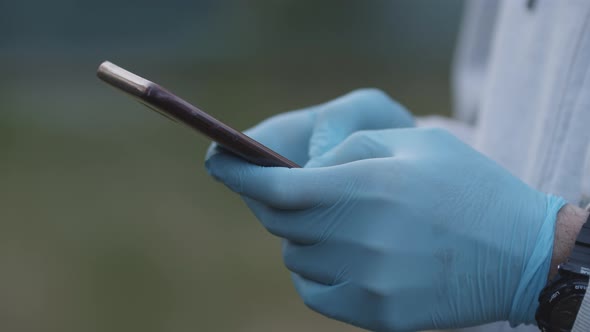 Slow Motion Close Up of Man Hands in Latex Gloves Typing Message on Mobile Phone