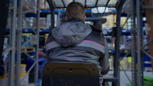 Back View Forklift Driver Riding Along Rows in Industrial Warehouse with Employees Standing Talking