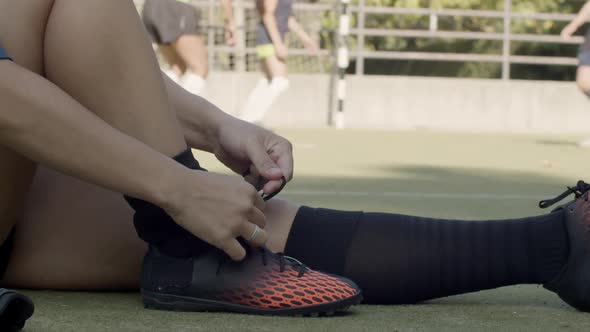 Side View of Female Football Player Lacing Up Shoes at Stadium