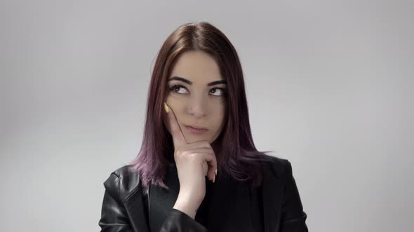 Young Woman with Violet Hair is Thinking Hard and Holds Her Face with Her Hand