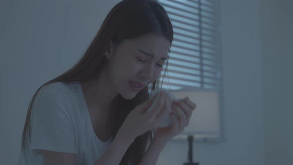 Asian sick girl in pajamas wake up from sleep at night sneezing on bed