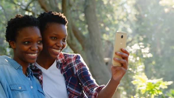 Twin sisters taking selfie with mobile phone in the park 4k