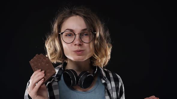 Close Up Brunette Young Woman with Glasses and Headphones Posing Playfully Eat Chewing Chocolate Bar