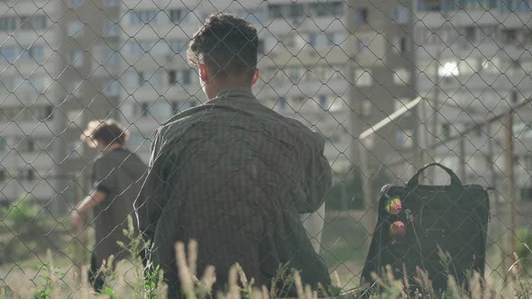 Back View of African American Man Sitting Behind Mesh Fence and Looking at Guys Playing Football