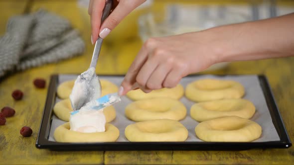 Woman cooks in the kitchen sweet open buns with cottage cheese, raspberries and shtreyzelem