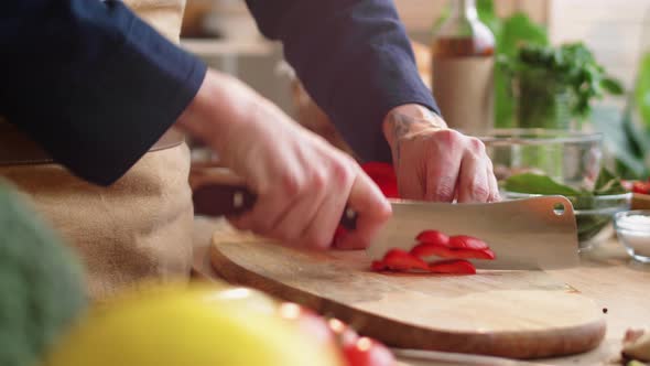 Male Cook Slicing Red Bell Pepper on Wooden Cutting Board