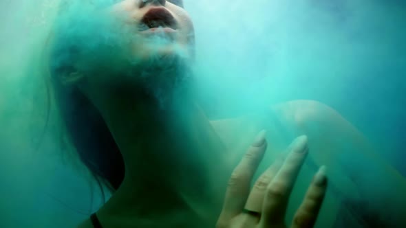 Graceful Lady is Floating in Mysterious Colored Smoke or Mist in Aquarium Amazing Fairytale Shot