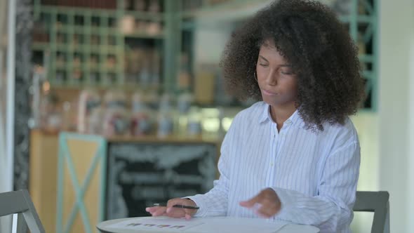 Serious Young African Businesswoman Doing Paperwork in Cafe