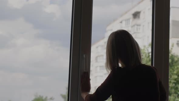 Back View A Woman Washes a Window in the Apartment of a Highrise Building